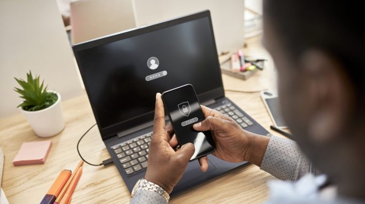 Businessman protecting data while using smart phone over laptop at office
