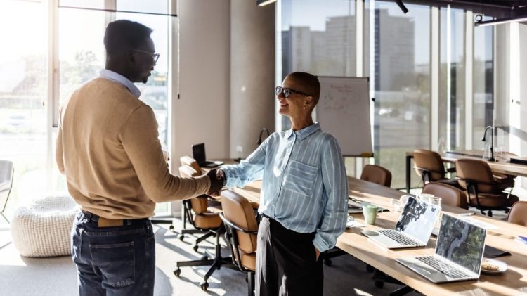 Photo of business partners shaking hands while standing in the office.