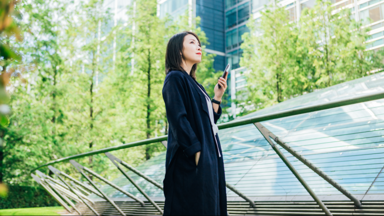 Woman standing in park with a cell phone in hand. Example of ESG initiatives at corporations