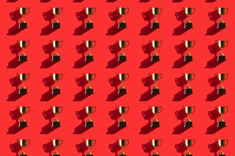 Pattern made of metallic golden goblets on red background with shadows. Flat lay style