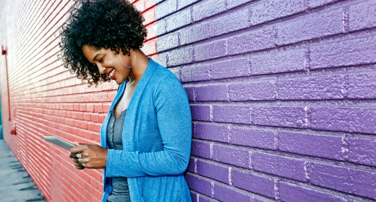 Woman leaning against wall looking at phone.