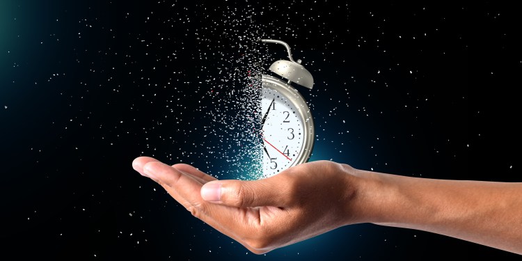 Concept of passing away, the clock breaks down into pieces. Hand holding analog clock with dispersion effect