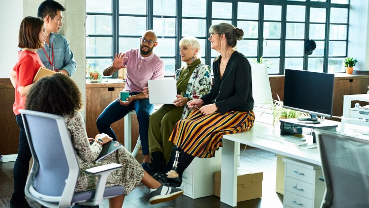 Colleagues in meeting with female amputee sitting on desk