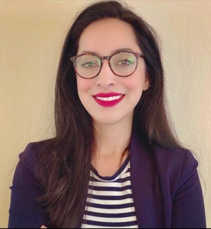 A woman with dark hair and glasses is smiling in a picture.
