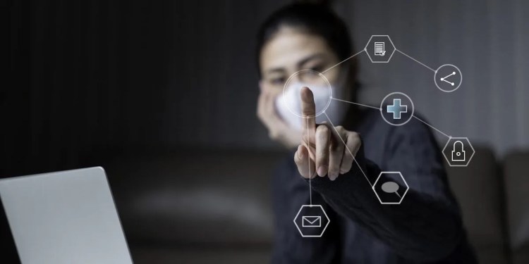 Asian woman wearing surgical mask on face protective for spreading of disease Covid-19 pandemic Coronavirus. Young Adult Asian using laptop while sitting on sofa with virtual graphic icon diagram.