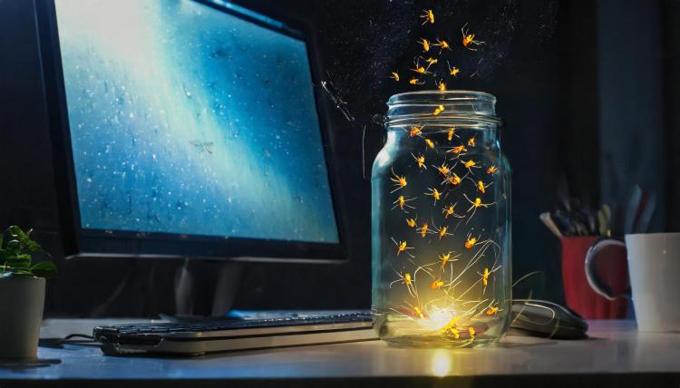 Fireflies escape a clear mason jar in front of a blue computer monitor.