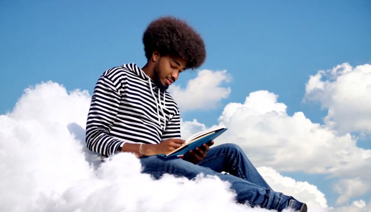 Screenshot from Hotshot promo AI video showing dark skinned man with Afro reading a tablet seated on a cloud